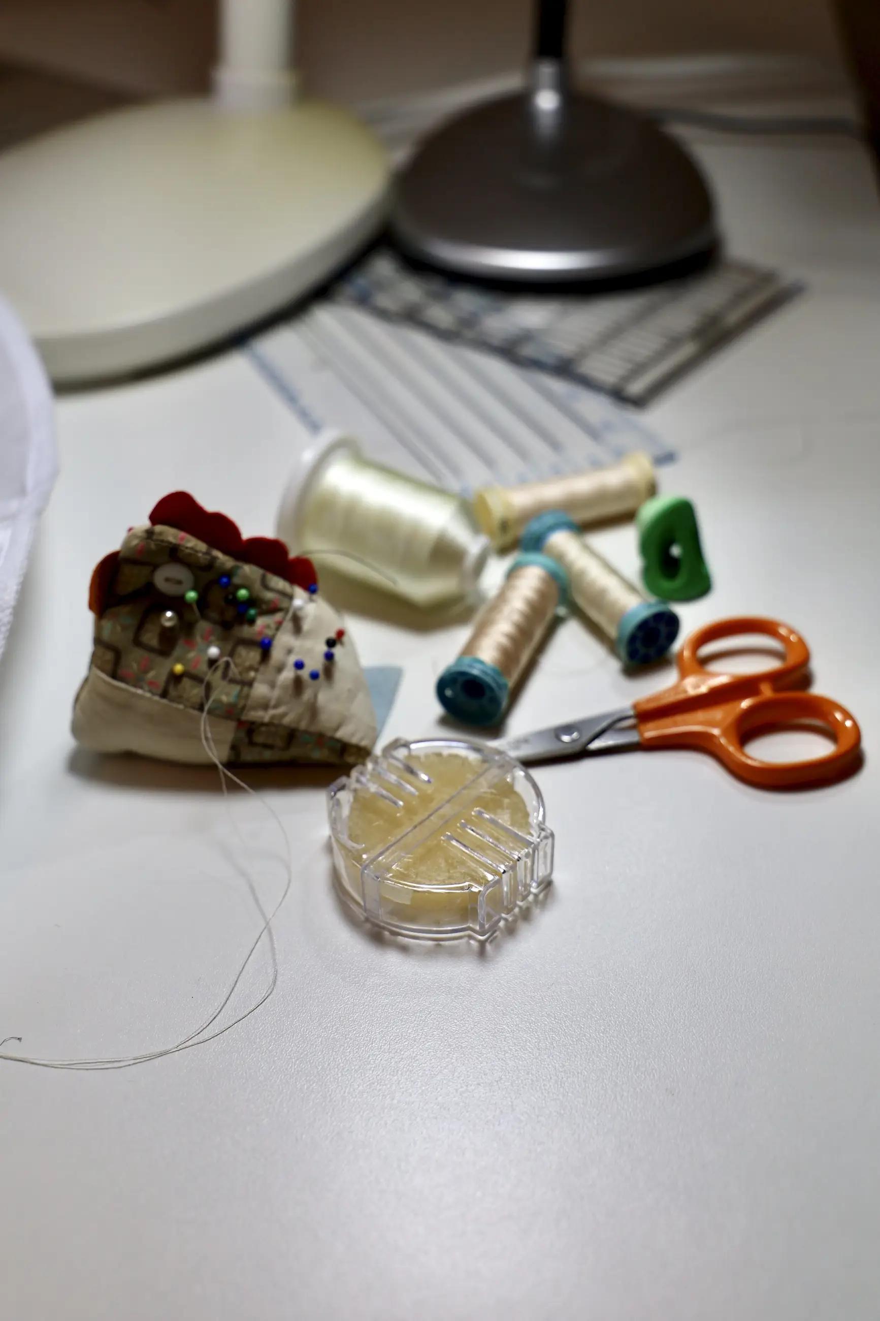 Tools for hand sewing: thin needles, pin cushion, various shades of thread, thimble, small scissors, and thread wax.